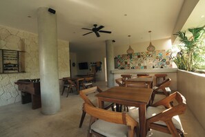 Uma área de refeições com mesas e cadeiras de madeira, um ventilador de teto e uma parede com um padrão de azulejos coloridos.