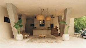 Quarto espaçoso com teto alto, grandes vasos de plantas, móveis de vime e um tapete estampado.