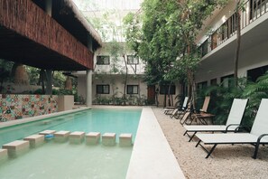 A swimming pool with steps leading into it, surrounded by lounge chairs and greenery.