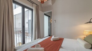 Una habitación de hotel con cama, ventana con cortinas, balcón y lámpara.