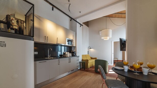 Una cocina moderna con armarios blancos, un microondas y un fregadero. Hay una zona de comedor con una mesa y sillas, y un sofá amarillo.