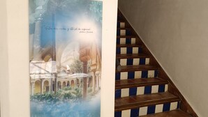 Una escalera con escalones de madera y franjas azules y blancas, que conduce a una pared con un cuadro de un edificio.