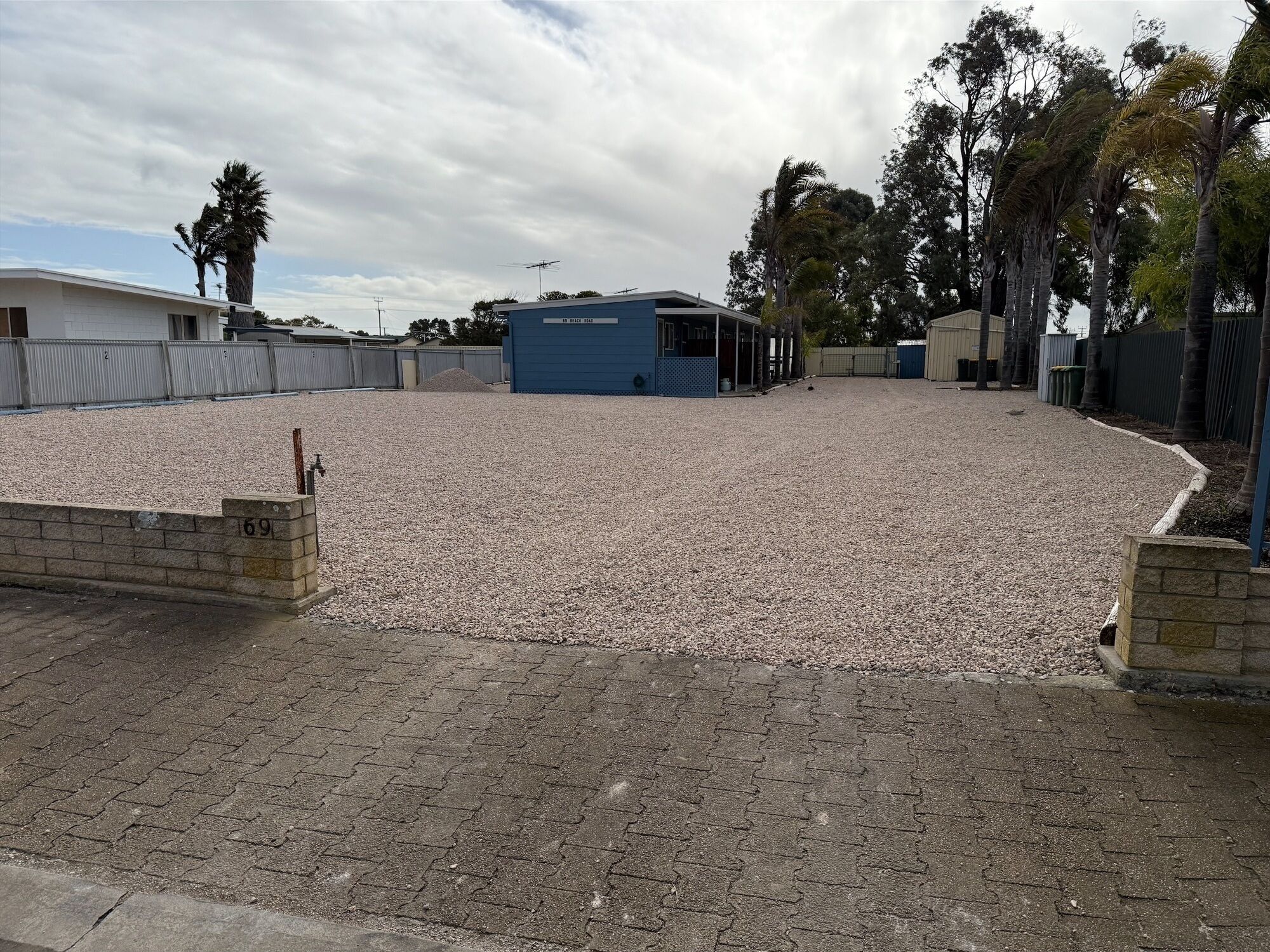 Un aparcamiento de grava con un edificio que dice "EL BARRIO 2013" al fondo.