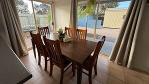 A dining area with a wooden table and chairs, a small plant, and a tissue box. - 3 by the Sea at Coobowie Unit 3 - 3 bedrooms - dog friendly-Off peak special! (Coobowie)