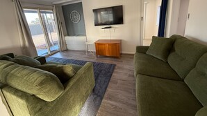 A living room with green sofas, a wooden coffee table, a flat-screen TV, and a large window with curtains. - 3 by the Sea at Coobowie Unit 3 - 3 bedrooms - dog friendly-Off peak special! (Coobowie)