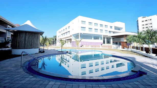 A swimming pool with a tiled deck, surrounded by modern buildings with large windows and a flat roof. - The Grand Rudraksh (Amravati)