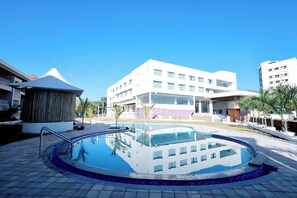 A swimming pool with a tiled deck, surrounded by modern buildings with large windows and a flat roof. - The Grand Rudraksh (Amravati)