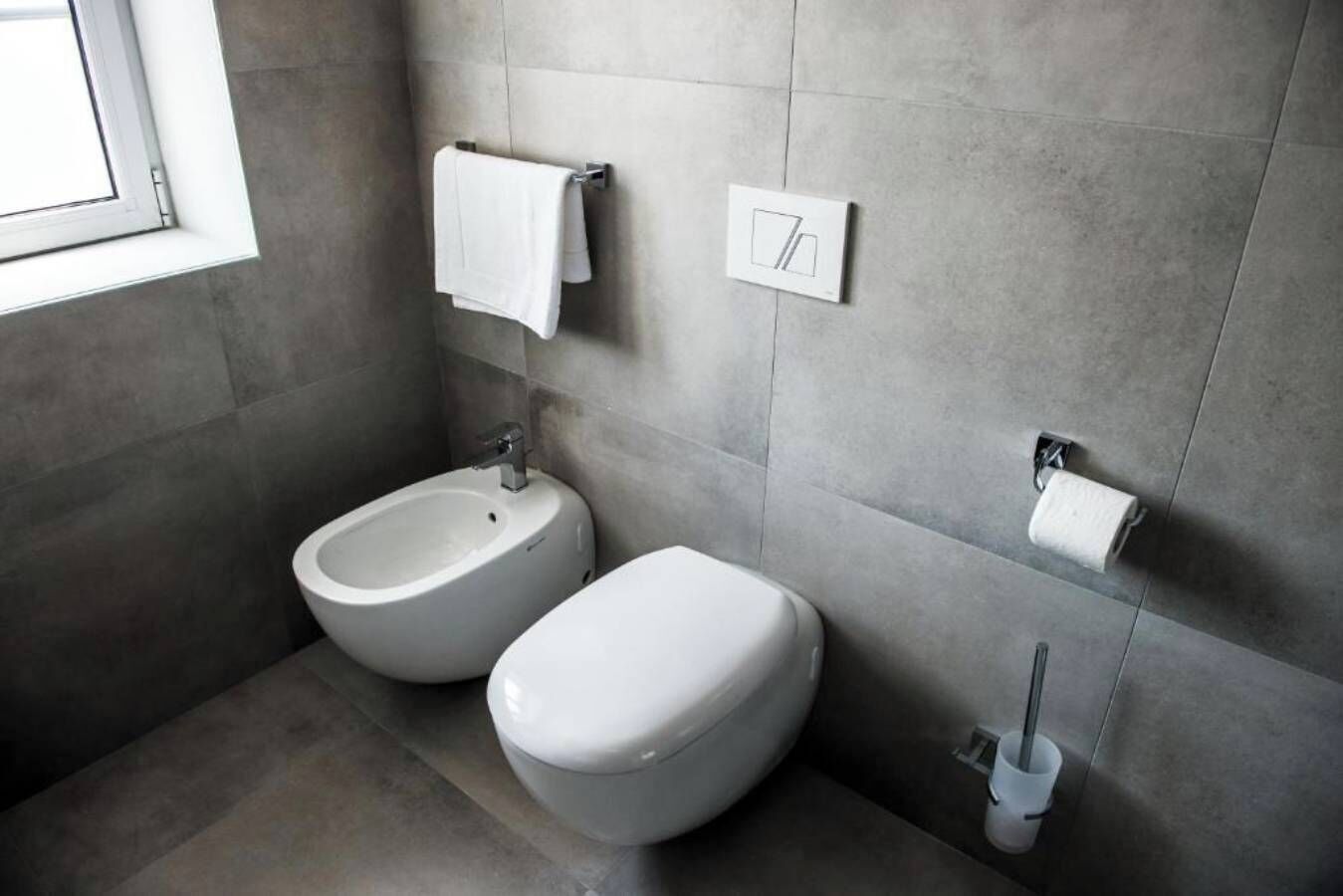 Une salle de bain moderne équipée de deux toilettes, d’un bidet, d’un porte-serviettes et d’un support à papier toilette.
