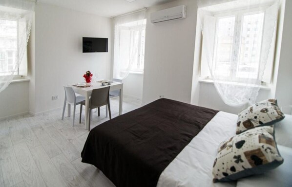 A bedroom with a bed, a desk, and a chair. - JOIVY Apartments - Trieste Goldoni (Trieste)