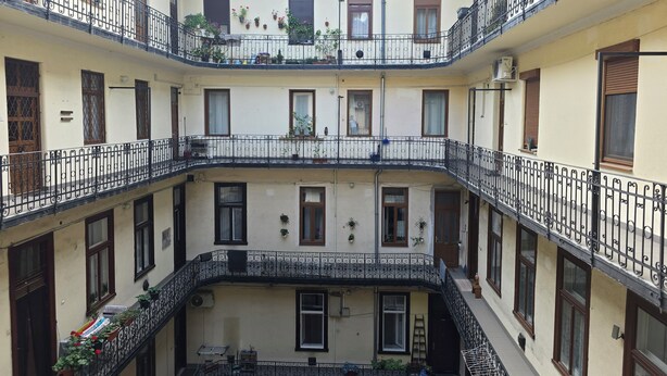 A multi-story building with balconies, potted plants, and a tiled roof.