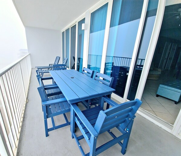 Un balcone con tavolo e sedie blu, ampie finestre e vista all'esterno.