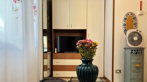 Un salón con televisor, un jarrón con flores, un sillón de peluche y un radiador.