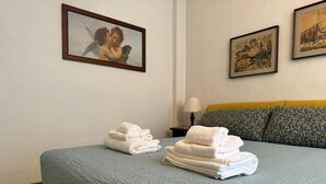 Una cama bien hecha con un edredón azul, una pila de toallas blancas y dos cuadros en la pared.