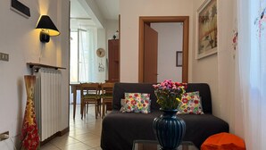 Una sala de estar acogedora con un sofá, una mesita de centro, un florero con flores, una lámpara y un radiador.