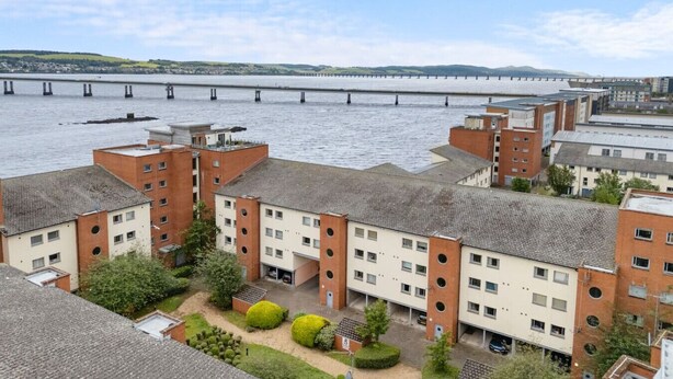 A residential building complex with multiple apartment buildings, a central courtyard, and a view of a bridge over water.