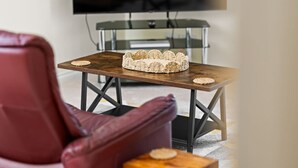 A modern living room with a leather armchair, a small wooden table with a woven basket, and a flat-screen TV mounted on the wall.