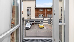 A view from a window overlooking a parking area with two cars, a building with a wooden facade, and a clear sky.