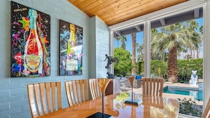 A dining area with a wooden table and chairs, a statue, and a pool view.