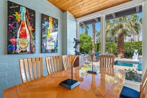 A dining area with a wooden table and chairs, a statue, and a pool view.