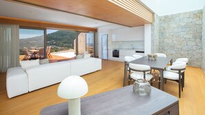 A modern living room with a large white sofa, a dining table with chairs, and a kitchen area with white cabinets.