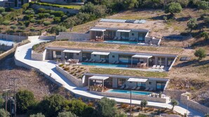 A modern villa with multiple swimming pools, stone architecture, and outdoor seating areas.