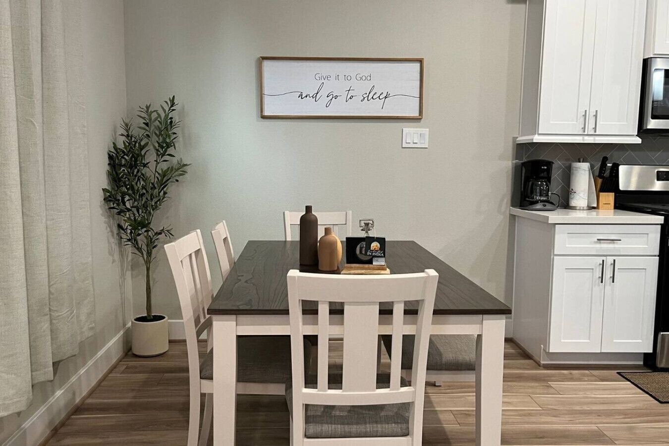 A dining area with a table, chairs, a potted plant, and a framed quote on the wall.