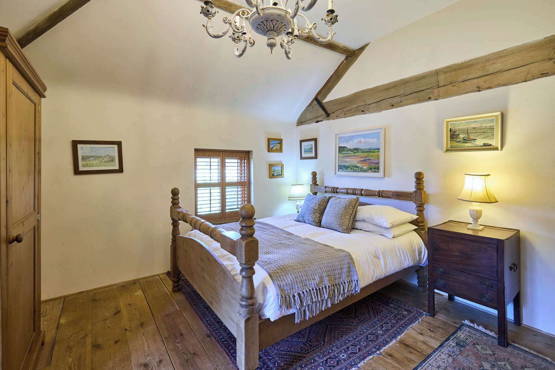 A bedroom with a wooden bed, a nightstand, a chandelier, and a window with shutters.