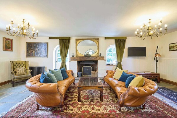 Ein traditionell eingerichtetes Wohnzimmer mit Ledersofas, einem gemusterten Teppich, einem Kamin und einem Fernseher.