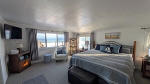 Un dormitorio con una cama grande, televisión, vistas a la playa y un pequeño rincón de descanso.