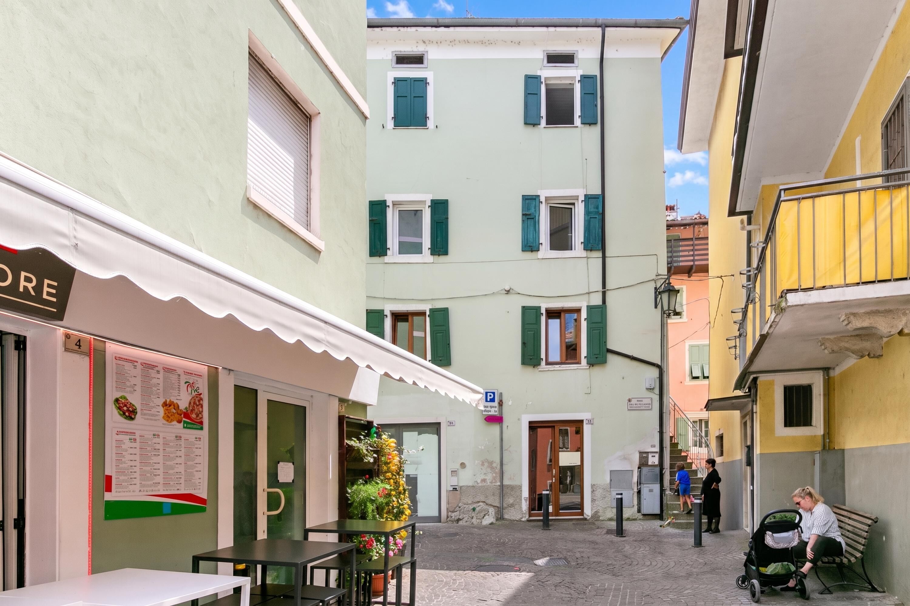 Eine enge Straße mit Häusern an beiden Seiten, ein Café mit Außenbestuhlung und ein Fußweg.