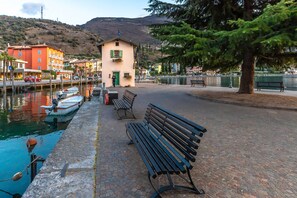A waterfront promenade with benches, a small building, and boats docked by the water. - Piccola Torbole 2min to Lake (Nago-Torbole)