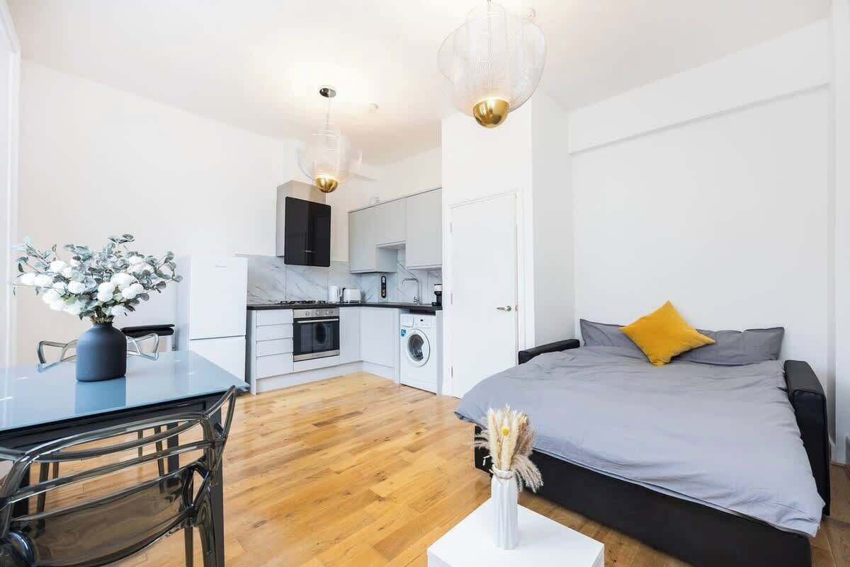 Een modern appartement met een eethoek, kitchenette en een bed met grijs en geel kussen.