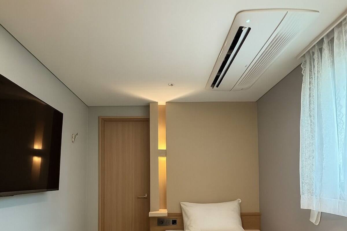 A hotel room with a bed, a desk, a television, and a ceiling-mounted air conditioner.
