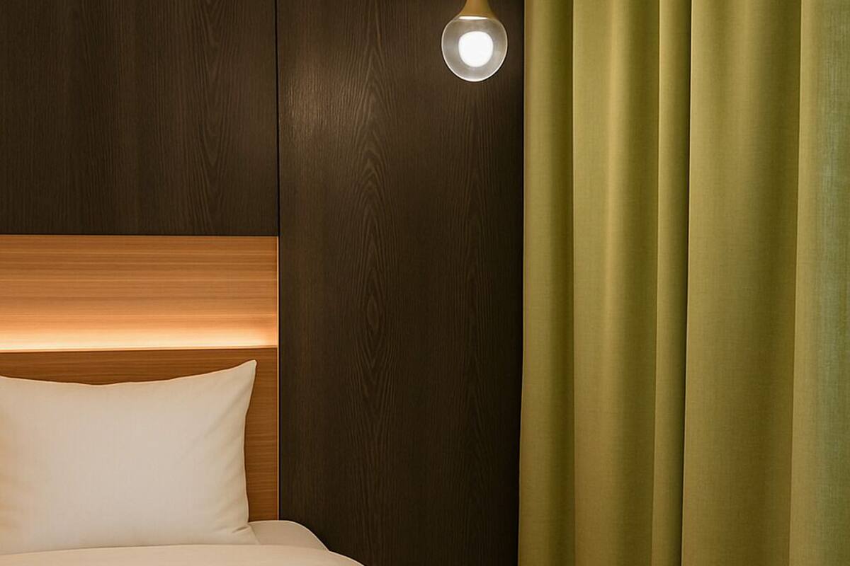 A hotel room with a wooden headboard, a bed with white bedding, a hanging light fixture, and green curtains.