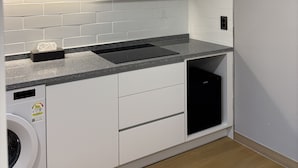A modern kitchen with white cabinets, a granite countertop, a built-in dishwasher, and a washing machine. - Seoul DDJ STAY (Seoul)