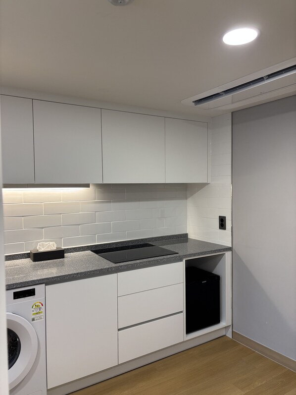 A modern kitchen with white cabinets, a granite countertop, a built-in dishwasher, and a washing machine. - Seoul DDJ STAY (Seoul)