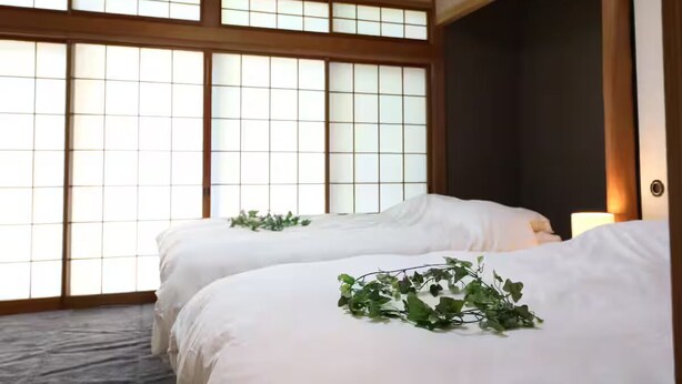 Perinteinen japanilaistyylinen huone, jossa on tatamimatto, paperiset shoji-liukuovet ja sänky, joka on koristeltu vihreällä kasvilla.