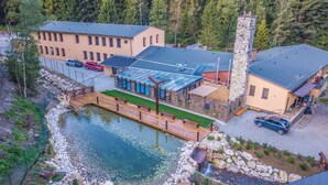 A lodge with a pond, a stone tower, and a glass-enclosed dining area. - Lopušná dolina Resort (Lučivná)