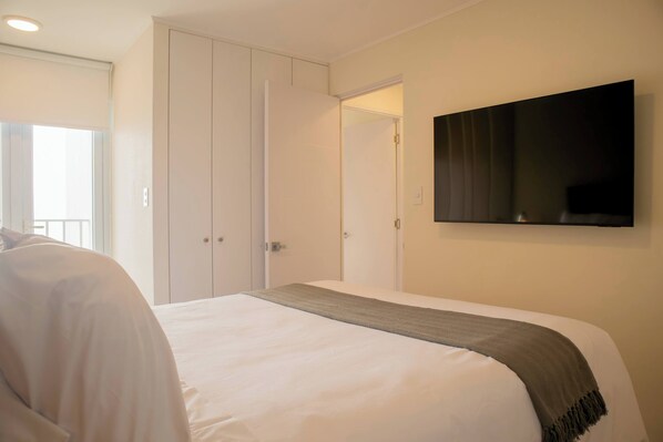 Quarto de hotel com cama, televisão na parede e guarda-roupa.