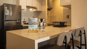 A modern kitchen with a stainless steel refrigerator, a built-in oven, and a large island with bar stools. There are two bottles of water and a box of bottled water on the island. - w Trendy 2BR Apartment w Pool in Barranco (Lima)
