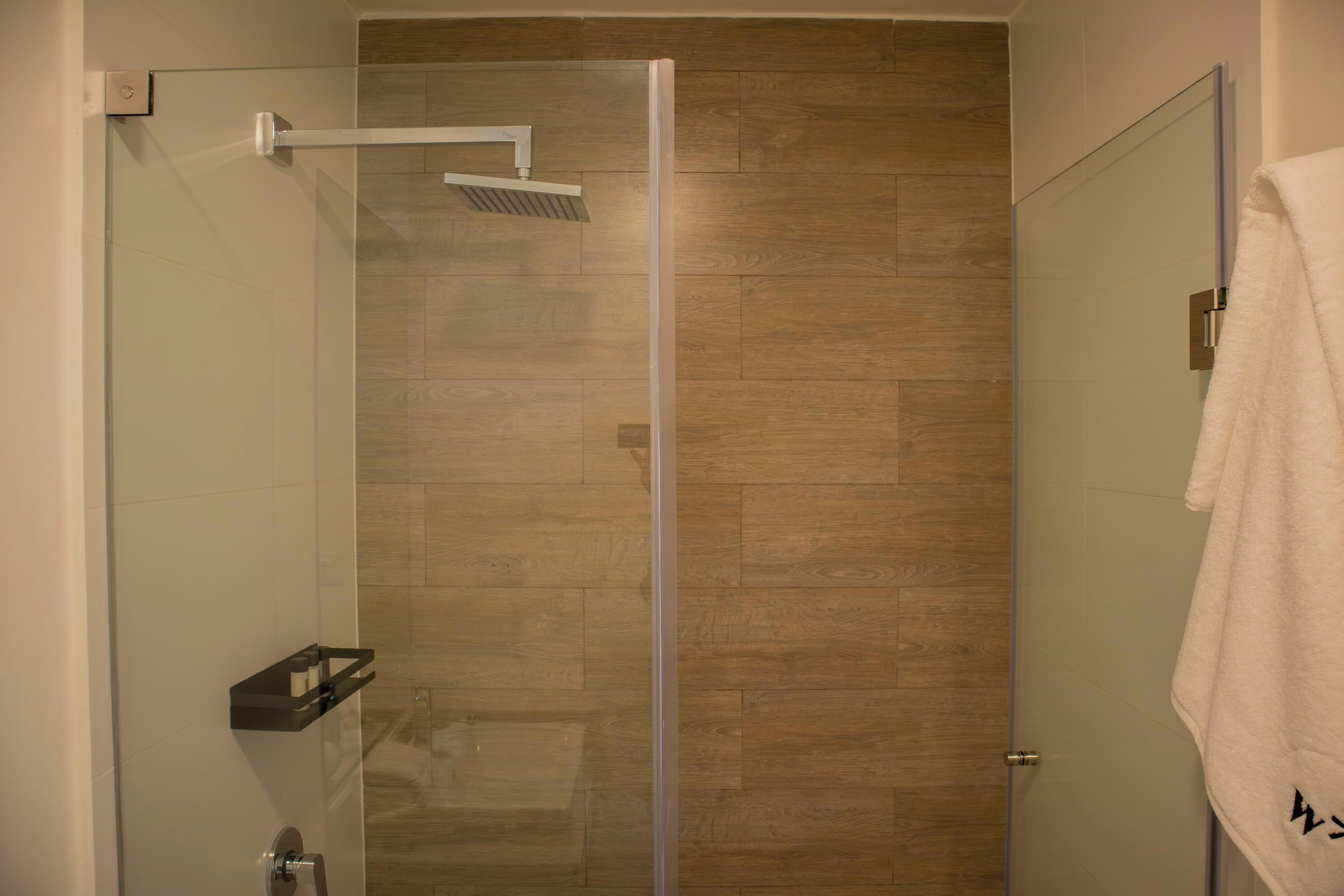 A glass-enclosed shower with a wooden floor, a towel rack, and a door with a towel hanging on it.