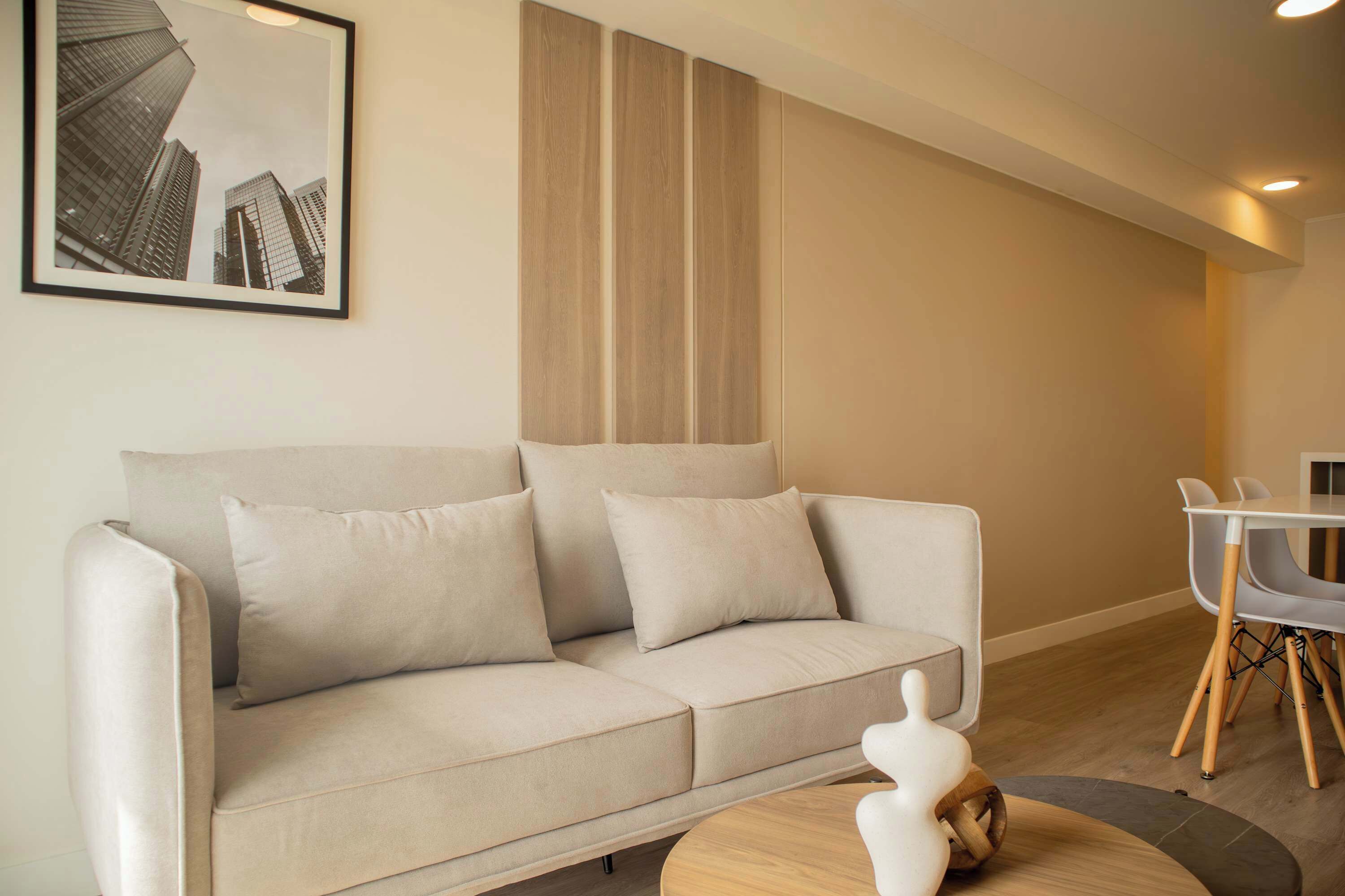 A modern living room with a beige sofa, a round wooden coffee table, and a framed cityscape picture on the wall.