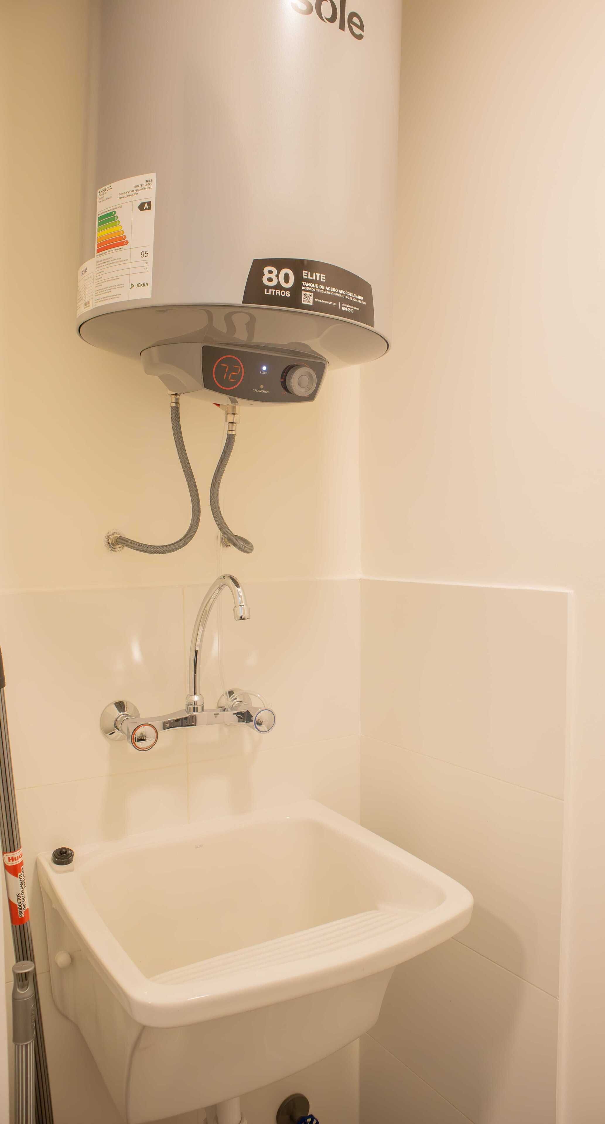 Un baño con un lavamanos blanco, un cabezal de ducha de mano y un calentador de pared etiquetado como '80 Litros'.