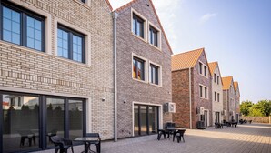 Een modern gebouw met een bakstenen gevel, grote ramen en een geplaveid binnenterrein met terras.