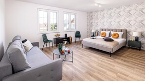 Een moderne slaapkamer met een bed, een bank, een klein tafeltje en twee stoelen. Er zijn ramen en een behang met een patroon.