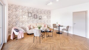 Een moderne woonkamer met een visgraat parketvloer, een beige bank, twee fauteuils, een salontafel en een bijzettafeltje met een bloevas.