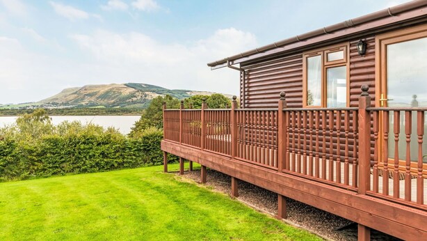 A wooden cabin with a balcony overlooking a lake and hills. - Wonderful private villa for 4 guests with WIFI, TV, balcony and pets allowed (Ballingry)