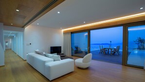 A modern living room with a white sofa, a TV, and a dining area with a table and chairs. - 2S Villas Resort - cave villas - Villa Epsilon E - Luxury Comfort Stay (Sivota)