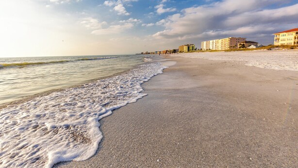 A beach with a sandy shore, waves, and buildings in the background.