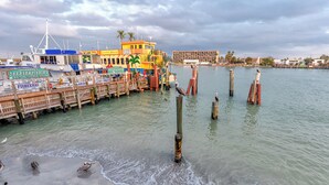 A waterfront area with boats docked, wooden posts in the water, and a building with a sign for a bait and tackle shop.